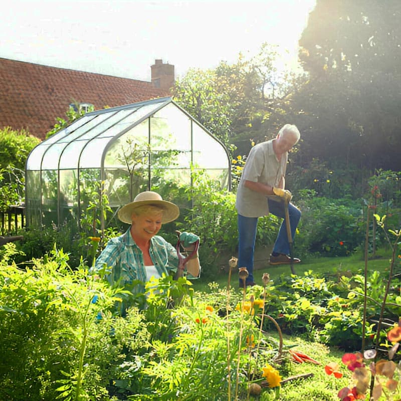 Pareja de ancianos arreglando jardín frente a un invernadero casero