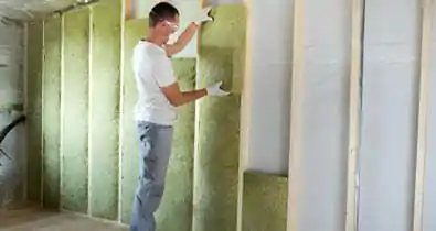 Hombre con gafas y cubrebocas instalando paneles de lana de roca en armazón de madera en pared - Insonorizantes